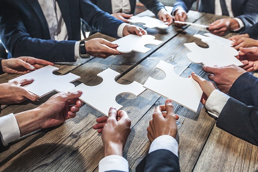 About Our Agency - Group Of Businessmen Holding Up Puzzle Pieces On Table